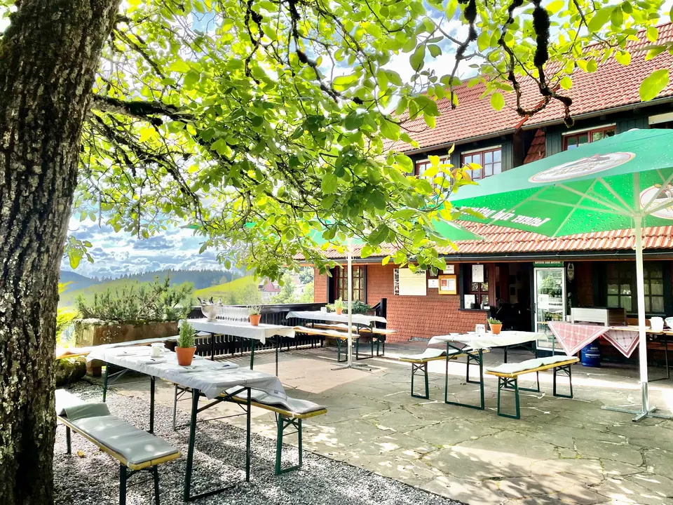 Biertische und grüne Sonnenschirme vor der Vesperstube mit Blick ins Tal