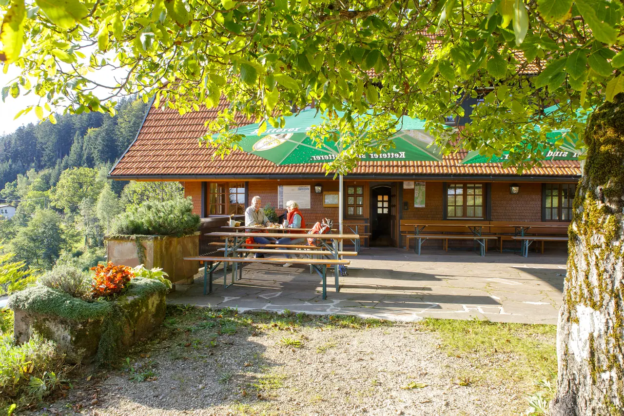 Das Schmalzerhisli mit Biergarten unter Bäumen, dahinter der Blick über die Wälder des Wolftals
